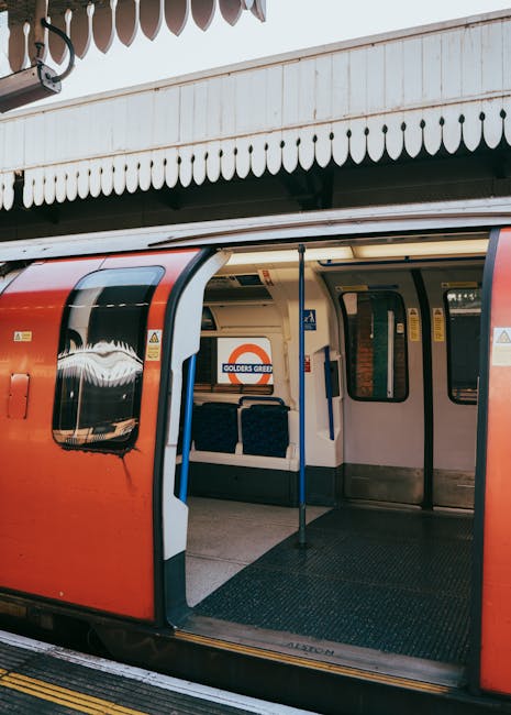 An empty interior of a commuter train carriage with a clean, polished floor and evenly spaced, patterned fabric seats along both sides. The carriage features yellow handrails and overhead handles for